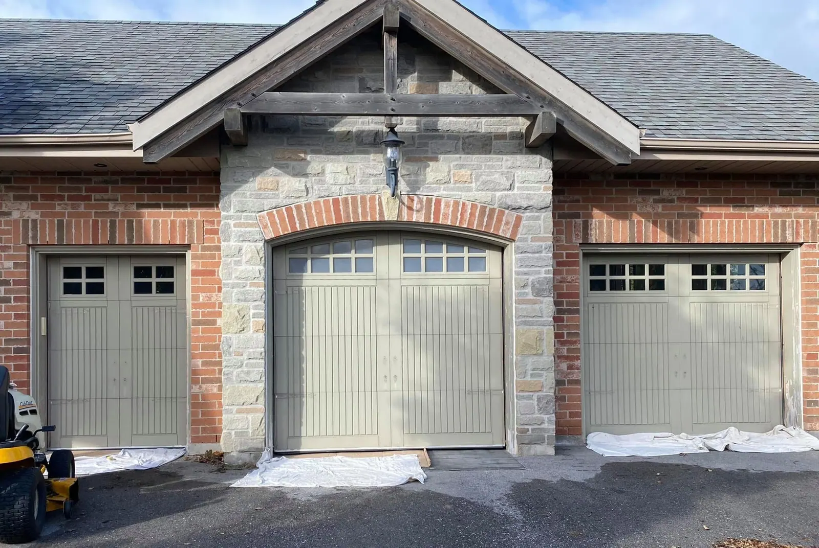 Garage doors painted a soft grey-green beside brick and stone