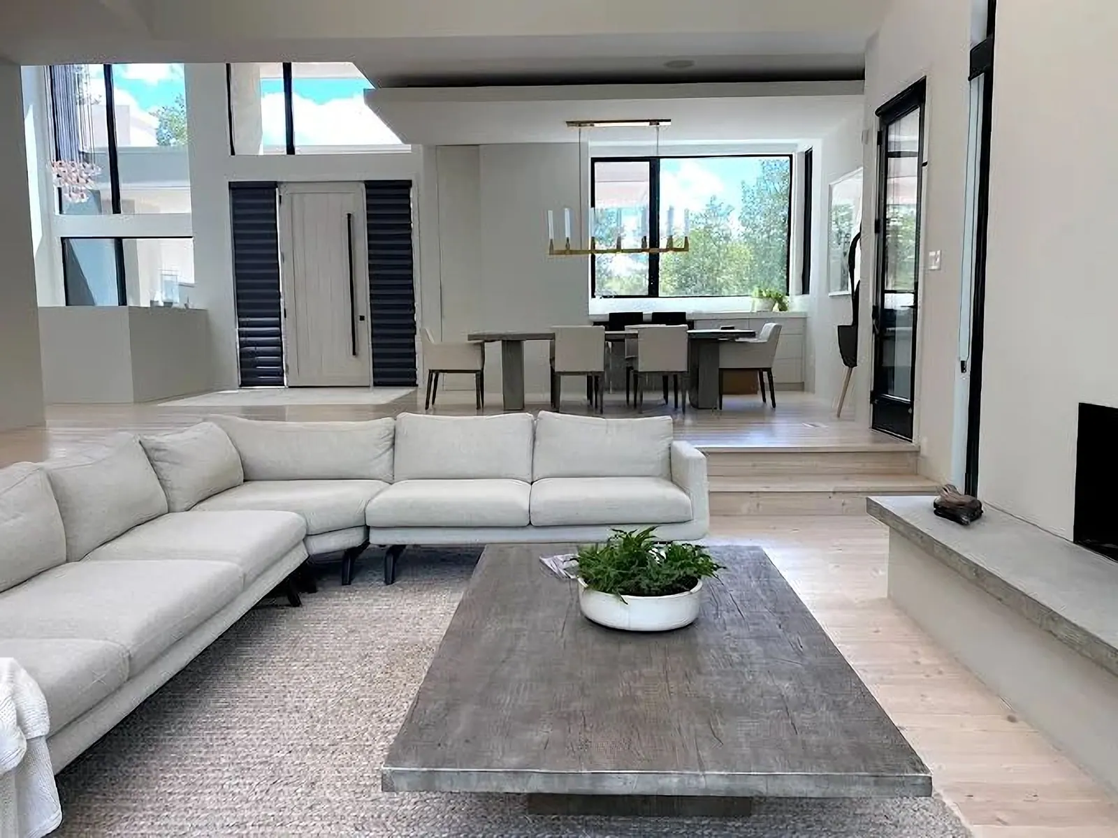 Open-plan living room with a pale sectional, a dining table and wide-plank floors
