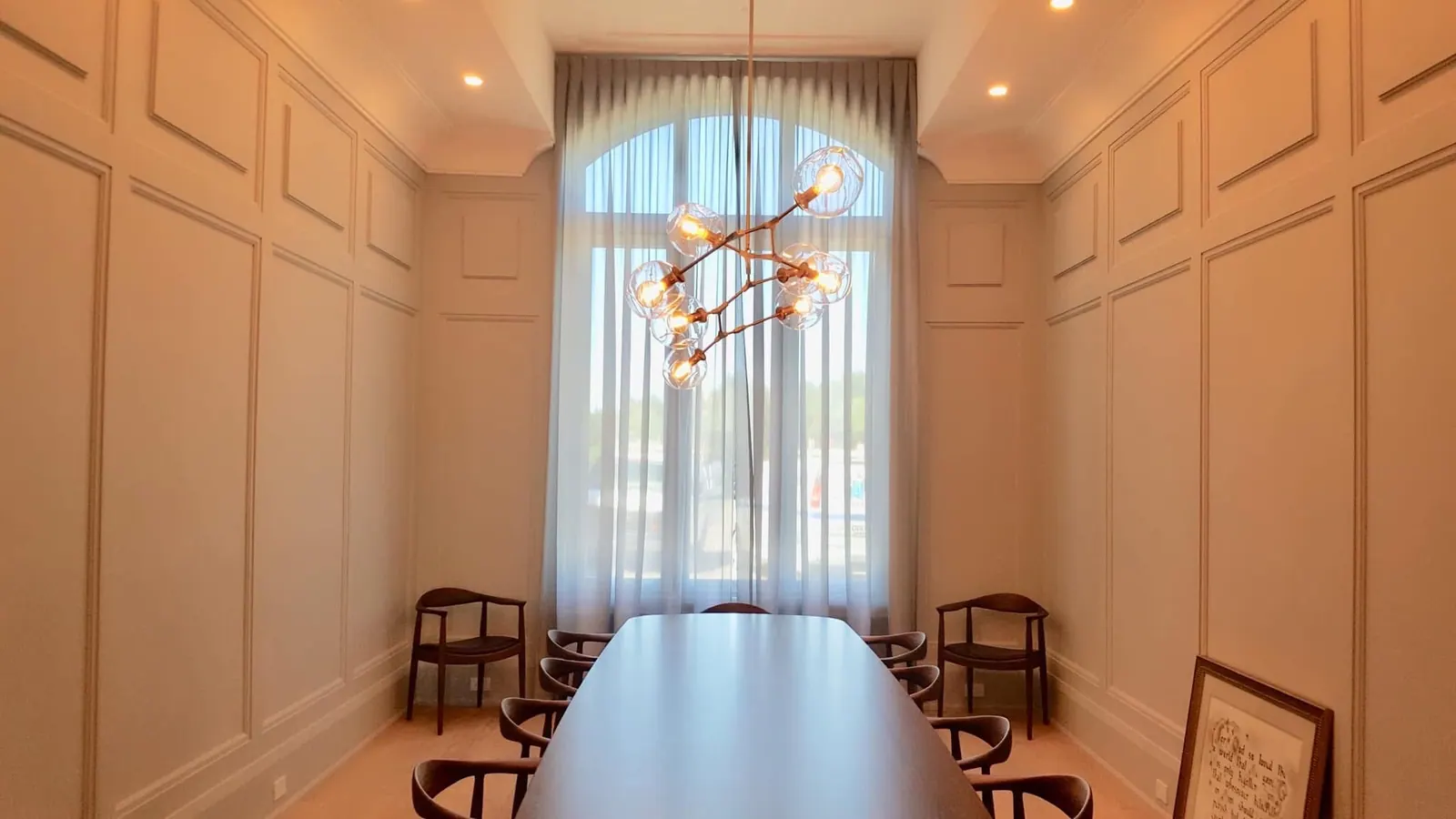Painted wall panelling beneath an arched window and a modern chandelier