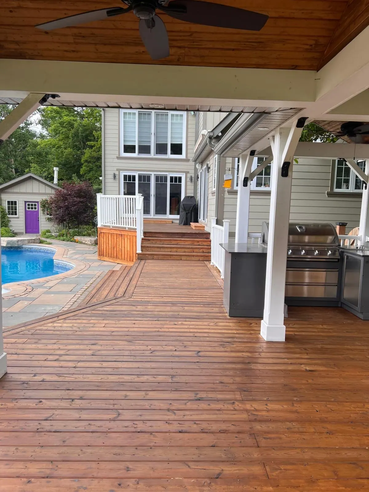 Stained pool deck with a white pergola and outdoor kitchen