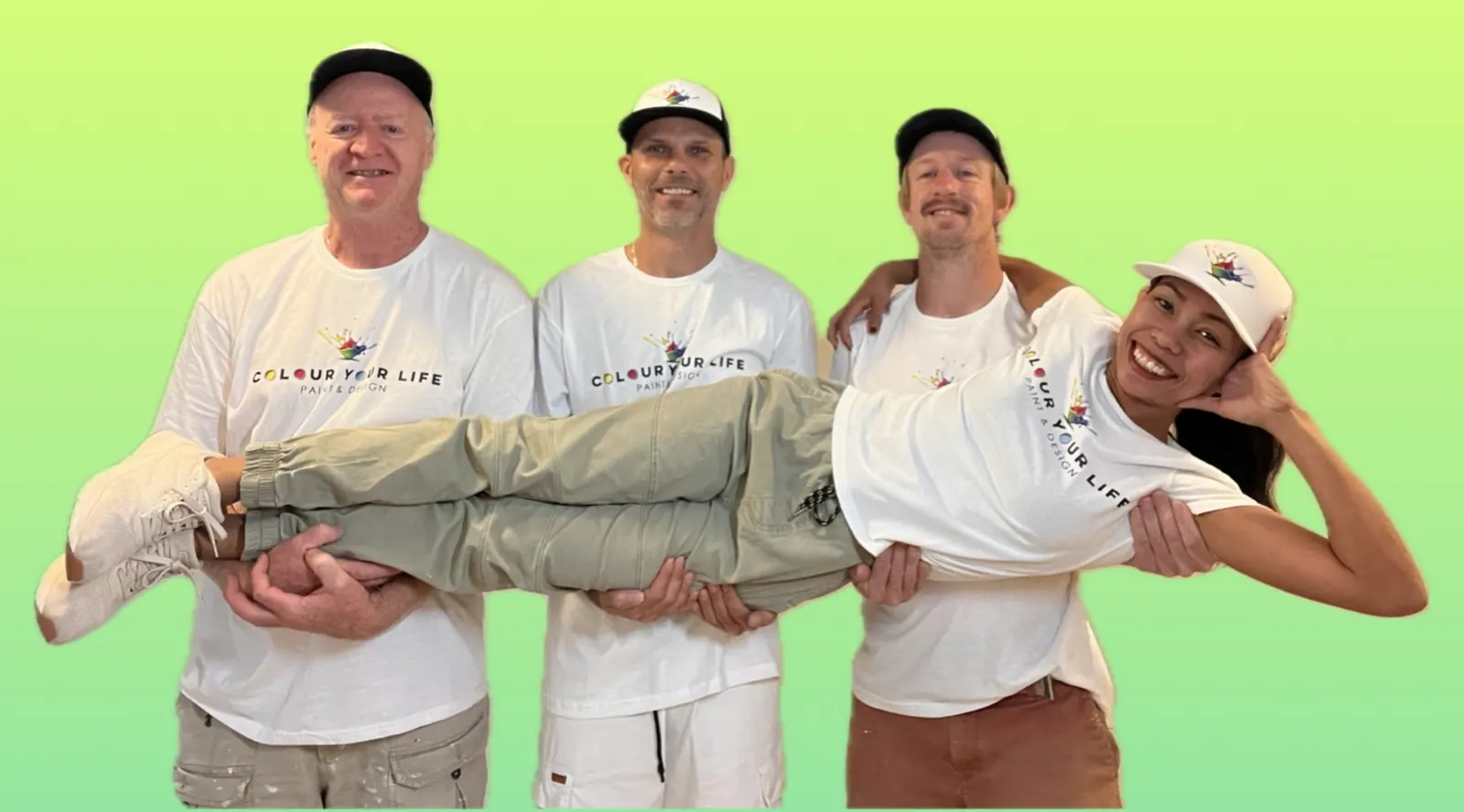 Four members of the Colour Your Life crew in matching white shirts and caps; three of them hold the fourth in the air, and everyone is smiling